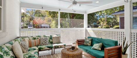 A covered porch with two sofas, a woven coffee table, and a ceiling fan.