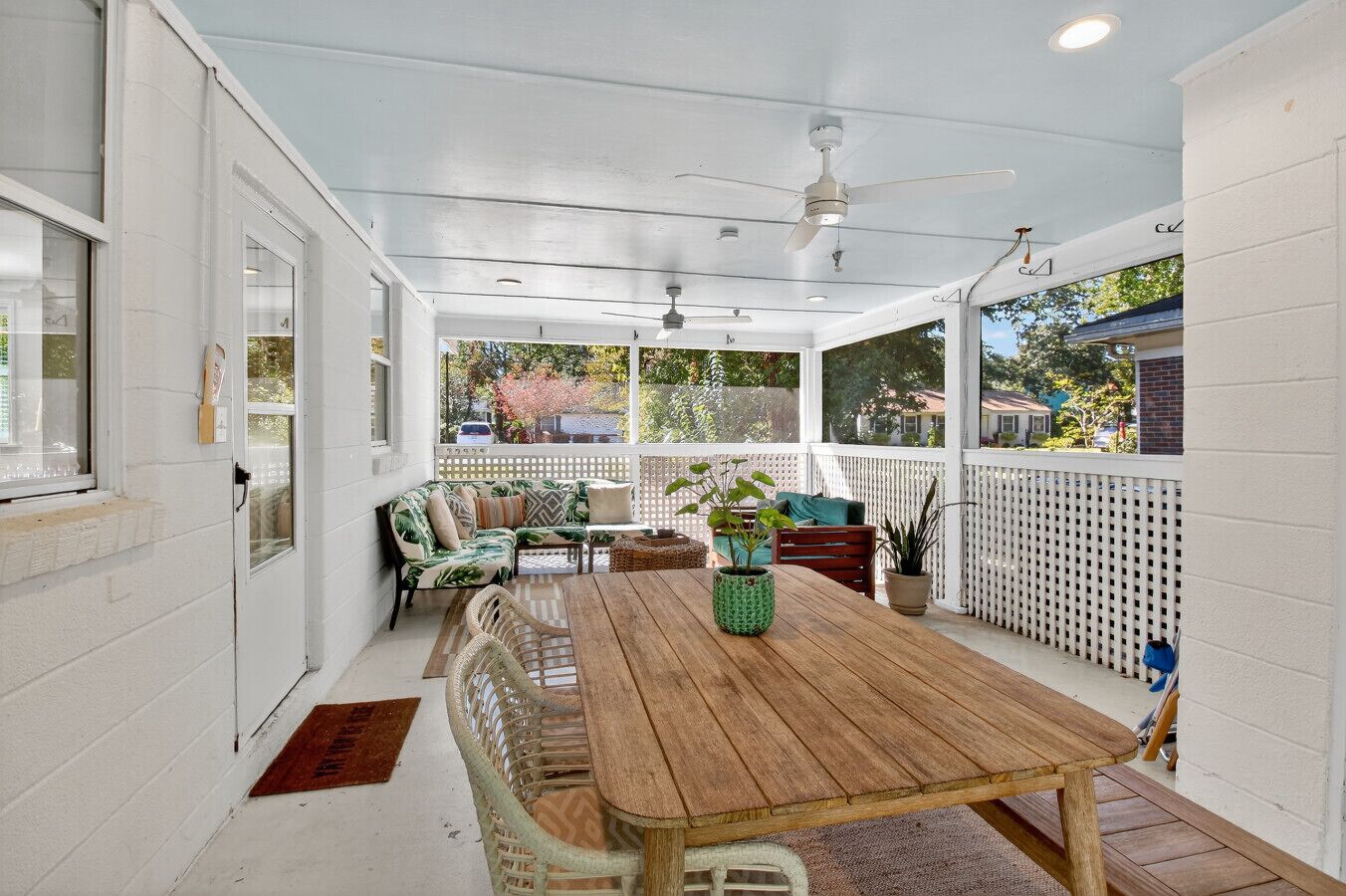 A covered patio with a wooden table, wicker chairs, and a white fence.