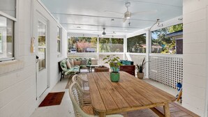 Eine überdachte Terrasse mit einem Holztisch, Korbstühlen und einem weißen Zaun.
