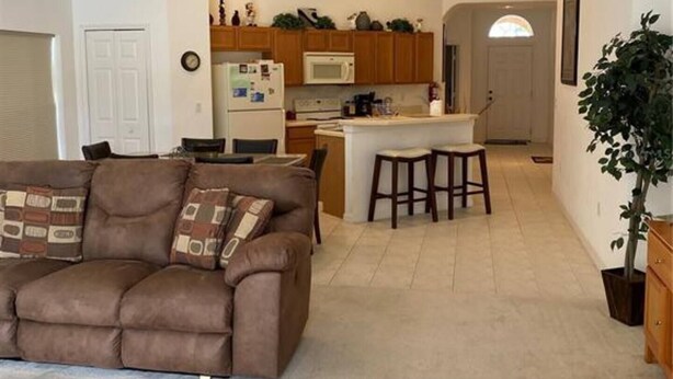 Una sala de estar moderna con un sofá marrón, un área de comedor y una cocina al fondo, además de un ventilador de techo.