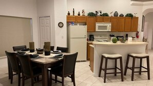 Una cocina moderna con armarios de madera, un refrigerador blanco, un microondas y una estufa. Hay una zona de comedor con una mesa y sillas.