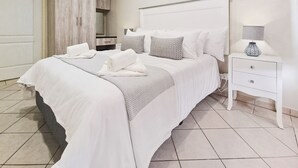 A neatly made bed with white linens and pillows, a bedside table with a lamp, and a wardrobe in the background. - Villa Mia - Two Bedroom Apartment, Sleeps 4 (Saint Lucia)