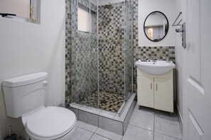 Un baño con ducha de mampara de vidrio, inodoro y lavabo con gabinetes.