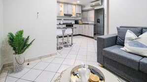 A modern kitchen with white cabinets, a dining area with a grey sofa and a small table, and a potted plant. - Villa Mia - Two Bedroom Apartment, Sleeps 4 (Saint Lucia)