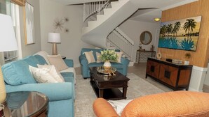 Una sala de estar con un sofá azul, un sillón naranja, una mesa de centro y una escalera.