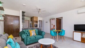 A modern living room with a green sofa, a grey couch, a round coffee table, and a dining area with blue chairs. - Serenity Escape (Mezcales)