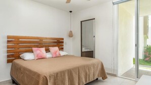 A bedroom with a wooden headboard, a bed with a beige blanket, two pillows, a hanging light fixture, and a sliding glass door leading to an outdoor area. - Serenity Escape (Mezcales)