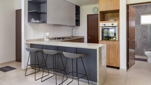 A modern kitchen with a central island, bar stools, a built-in oven, and a clock on the wall. - Serenity Escape (Mezcales)