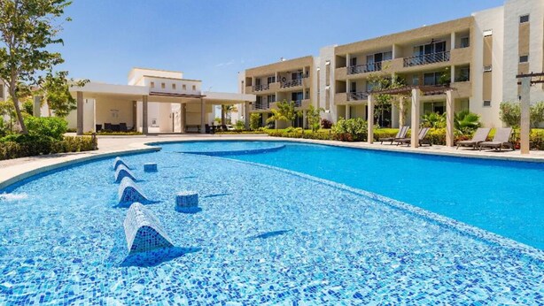 A swimming pool with mosaic tiles, surrounded by a building with multiple balconies and a covered area. - Serenity Escape (Mezcales)