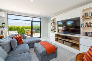 A modern living room with a sectional sofa, a flat-screen TV, and a bookshelf.