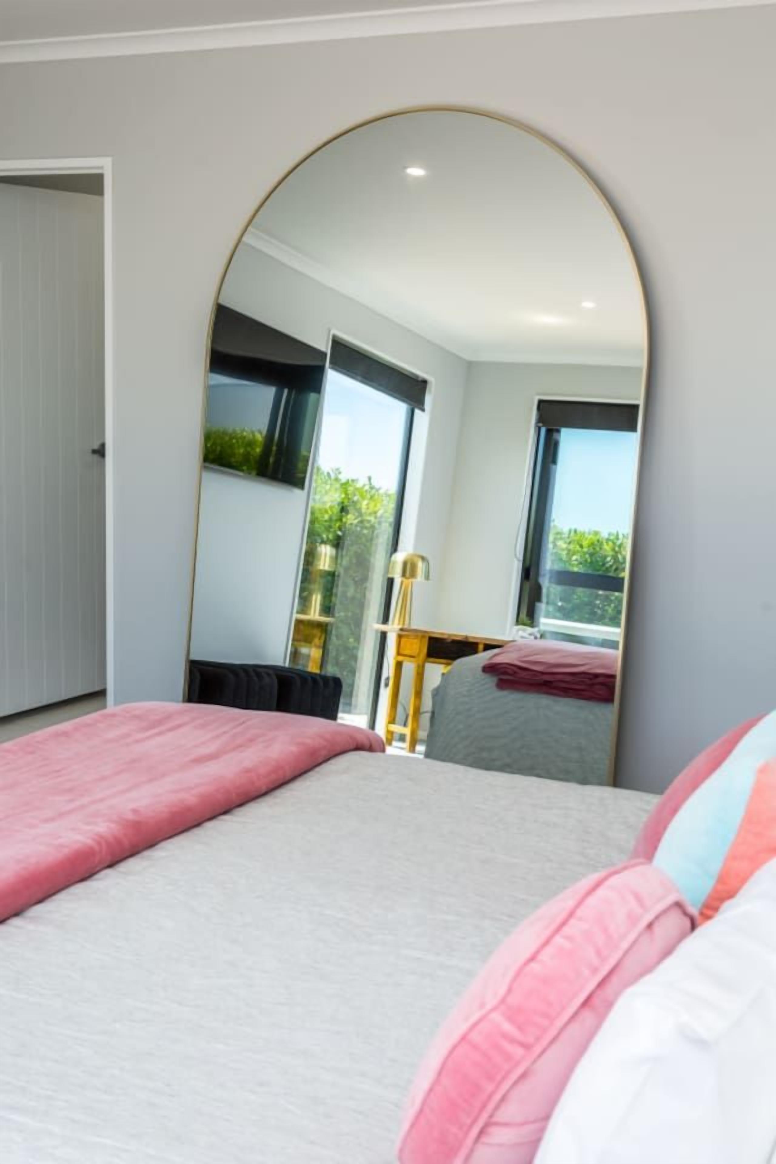 A bedroom with a bed, a large mirror, and a view of a balcony.