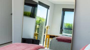 A bedroom with a bed, a large mirror, and a view of a balcony.