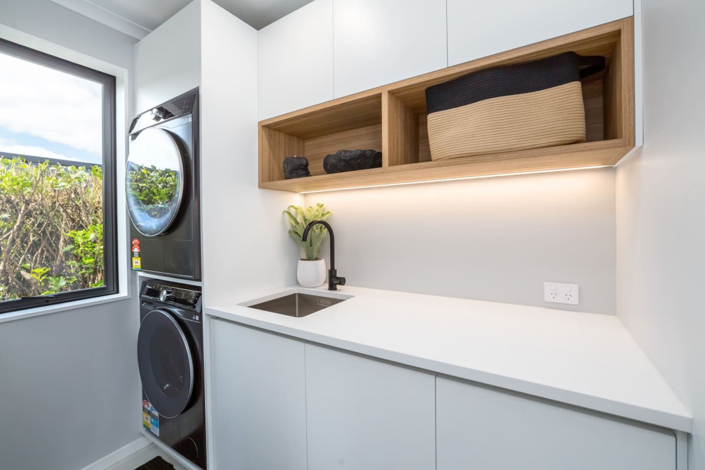 Une cuisine compacte équipée d’un lave-linge intégré, d’un évier et d’une étagère avec des paniers de rangement.