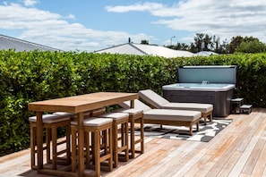 An outdoor deck with a wooden table and lounge chairs, a hot tub, and a hedge in the background. - Sotally Tober Retreat (Martinborough)