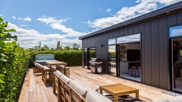A modern outdoor deck with a wooden table and chairs, a barbecue grill, and a sofa.