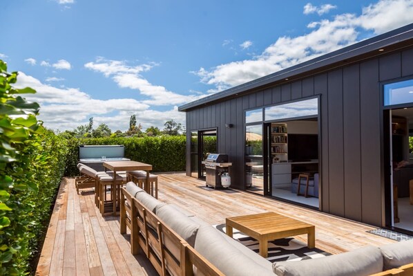 A modern outdoor deck with a wooden table and chairs, a barbecue grill, and a sofa. - Sotally Tober Retreat (Martinborough)