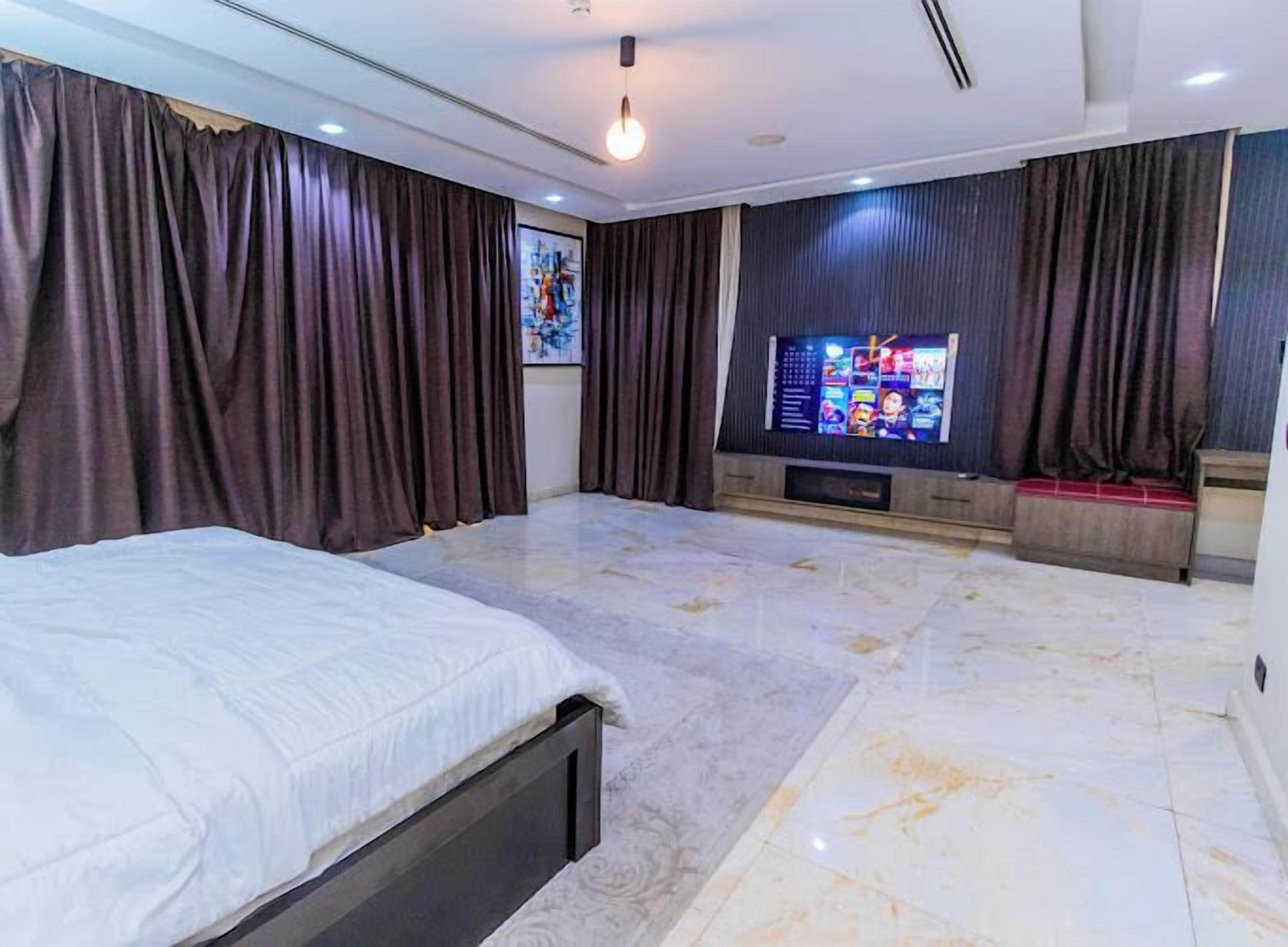 A modern bedroom with a large bed, a TV, and dark curtains.
