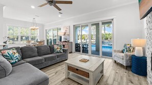 Ein geräumiges Wohnzimmer mit einem grauen Ecksofa, einem Holztisch und einem Deckenventilator.