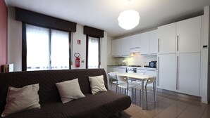 A modern living room with a brown sofa, a dining table with chairs, and a kitchen area with white cabinets and appliances. - Alby's apartment, in the Motor Valley with private parking (Formigine)