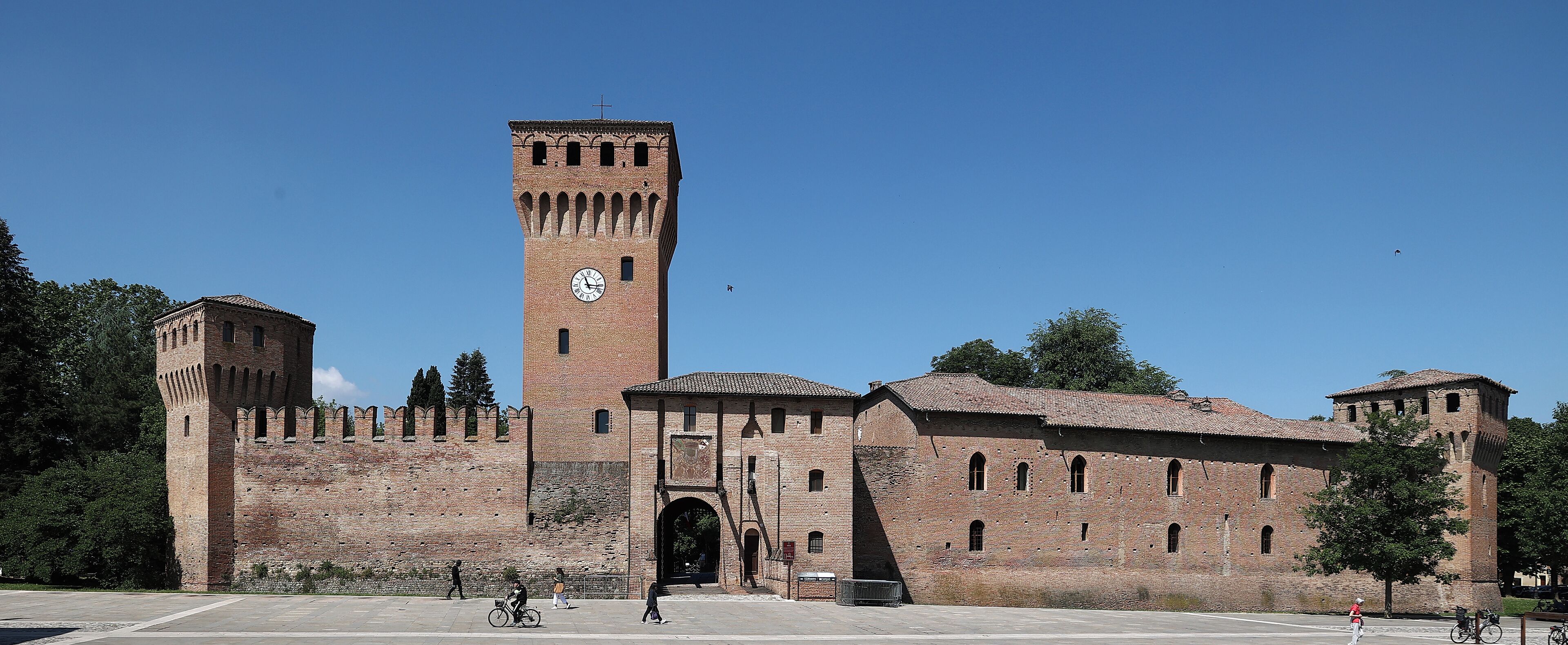 Un edificio storico in mattoni con una torre imponente e un ingresso ad arco.
