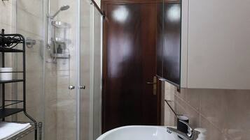 A bathroom with a glass-enclosed shower, a white sink, and a wooden door.
