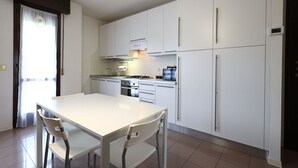 A modern kitchen with white cabinets, a stainless steel stove, and a dining area with a white table and chairs. - Alby's apartment, in the Motor Valley with private parking (Formigine)