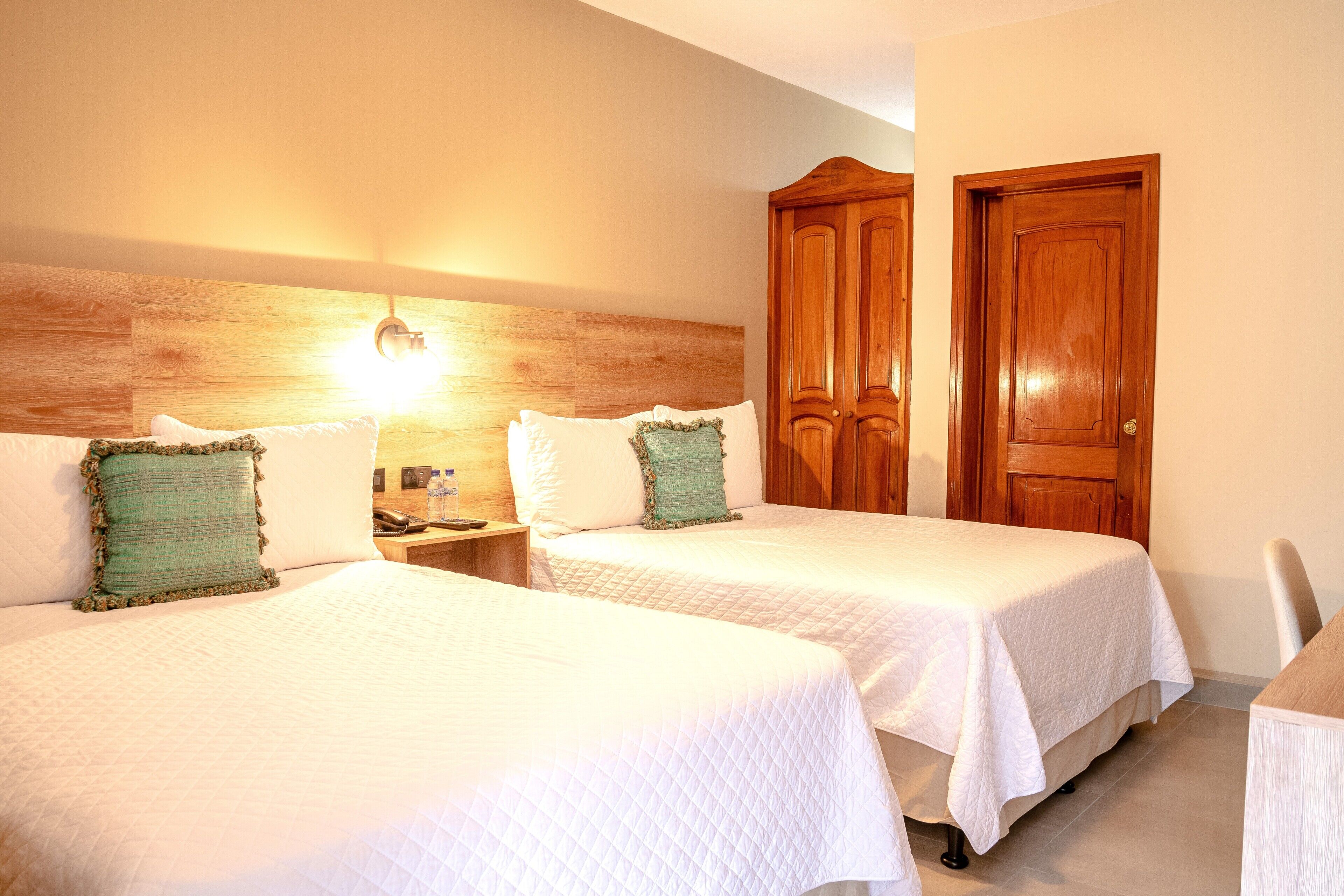 Una camera d'albergo con due letti, una testiera in legno, un comodino con un telefono e una porta in legno.