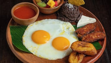 A plate with fried eggs, plantains, and a fruit bowl.