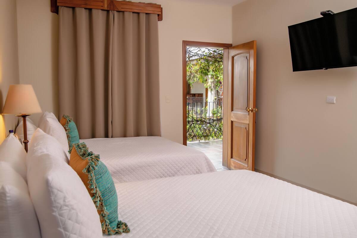 Habitación de hotel con dos camas, un televisor montado en la pared y vista al balcón exterior.