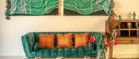 Un sofá verde con cojines naranjas, una mesa de centro de madera y un jarrón con flores.