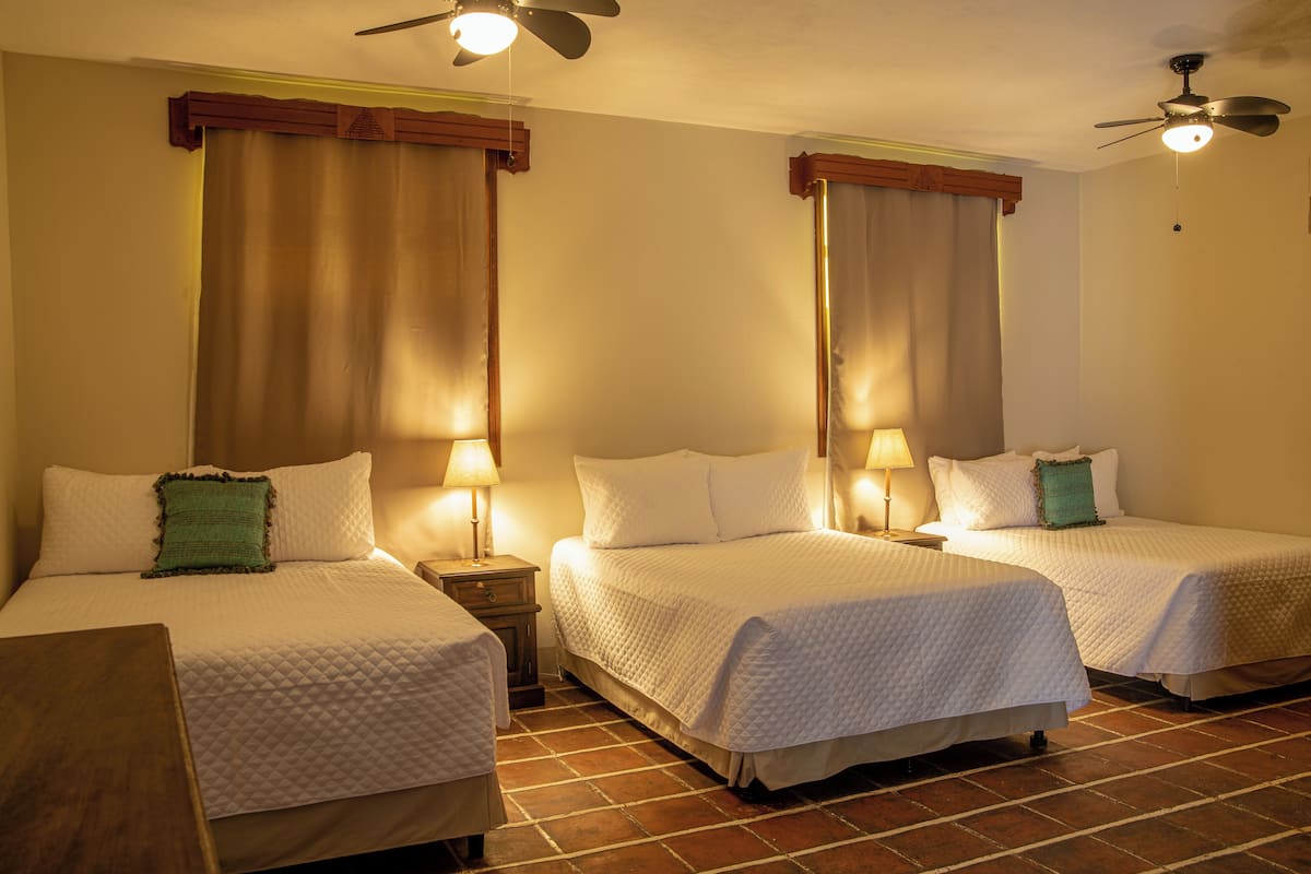 Una habitación de hotel con dos camas, cada una con un almohadón y una mesita de noche con una lámpara.