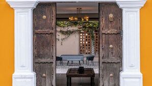 Entrada de un edificio con un letrero que dice "Casa Carmina", una puerta de madera, un banco y una mesa afuera.