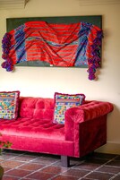Un sofá rojo con almohadones coloridos y una manta vibrante colgada encima.