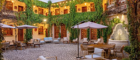 Un patio interior con suelo de piedra, varias zonas de estar y luces colgantes.