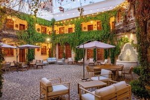 Un patio interior con suelo de piedra, varias zonas de estar y luces colgantes.