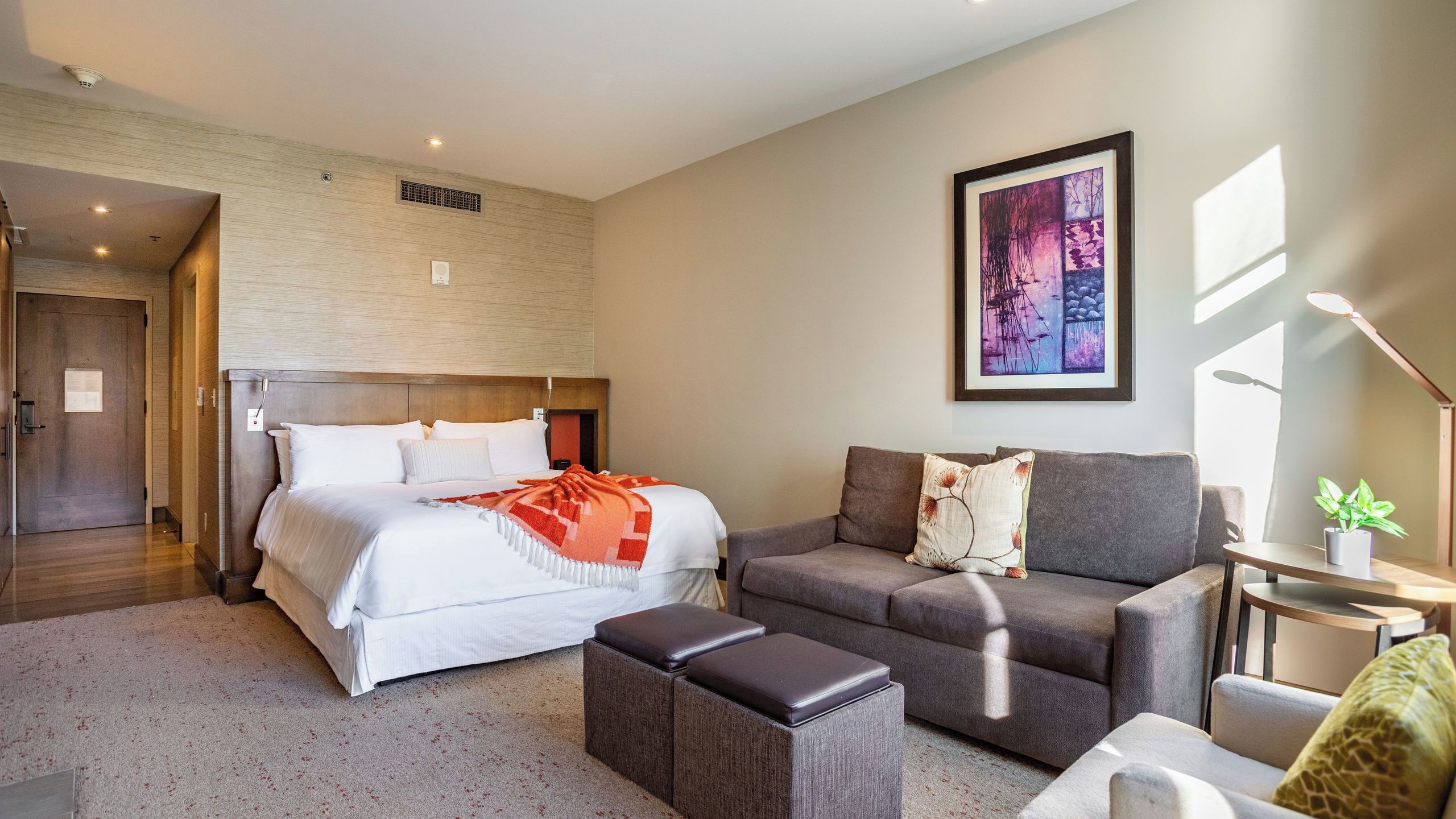 Una camera d'albergo moderna con un letto, un divano, un tavolino e un quadro appeso al muro.