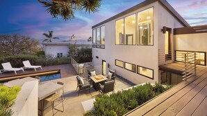 A modern house with a pool, outdoor seating, and a staircase leading to a deck.