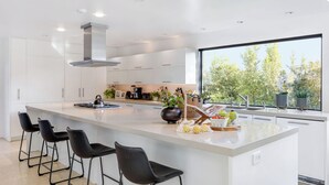 A modern kitchen with white cabinetry, a large island with bar stools, a gas stove, and a view of greenery outside.