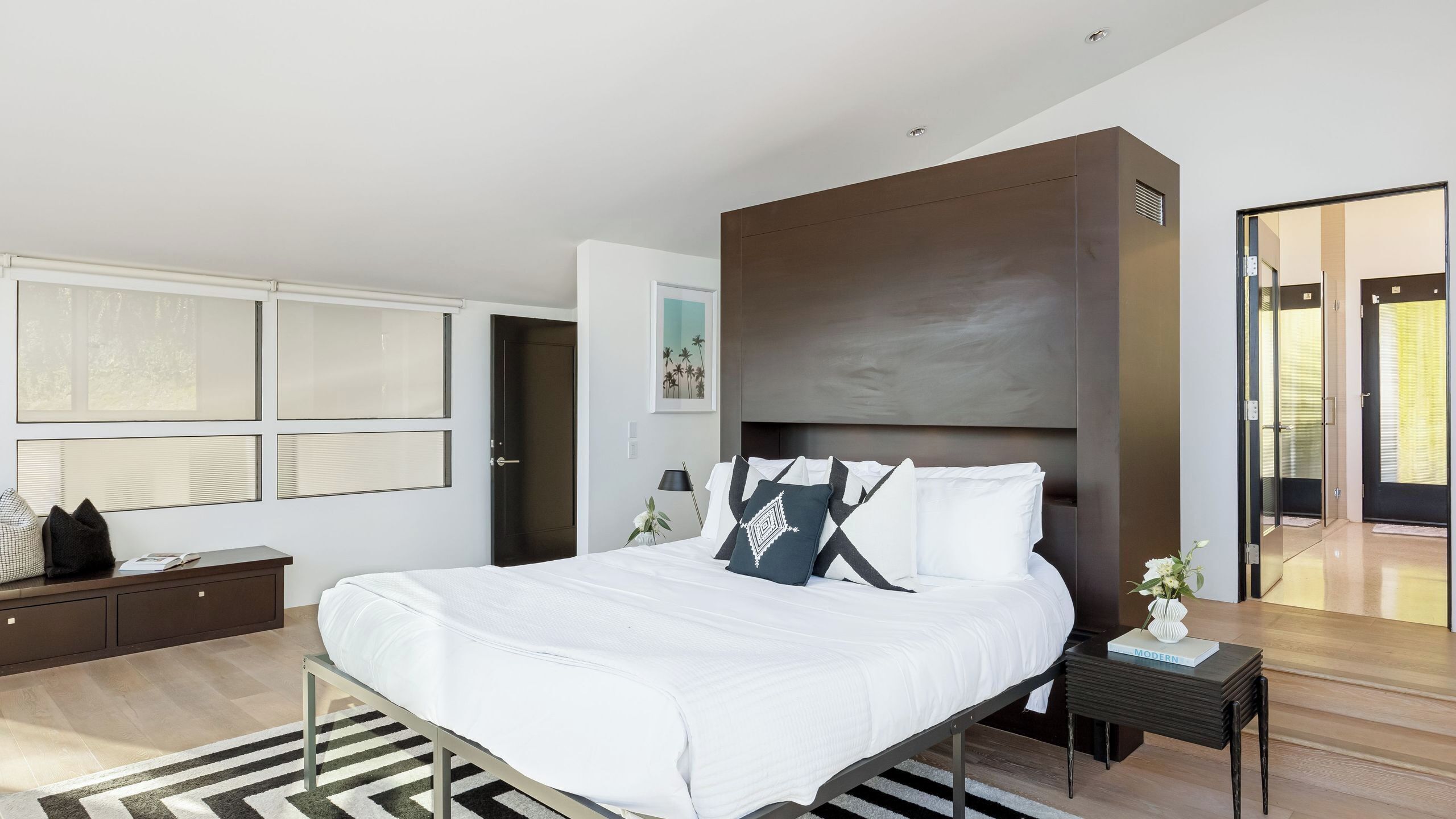 Een moderne slaapkamer met een groot bed, nachtkastjes en een raam met zonwering.