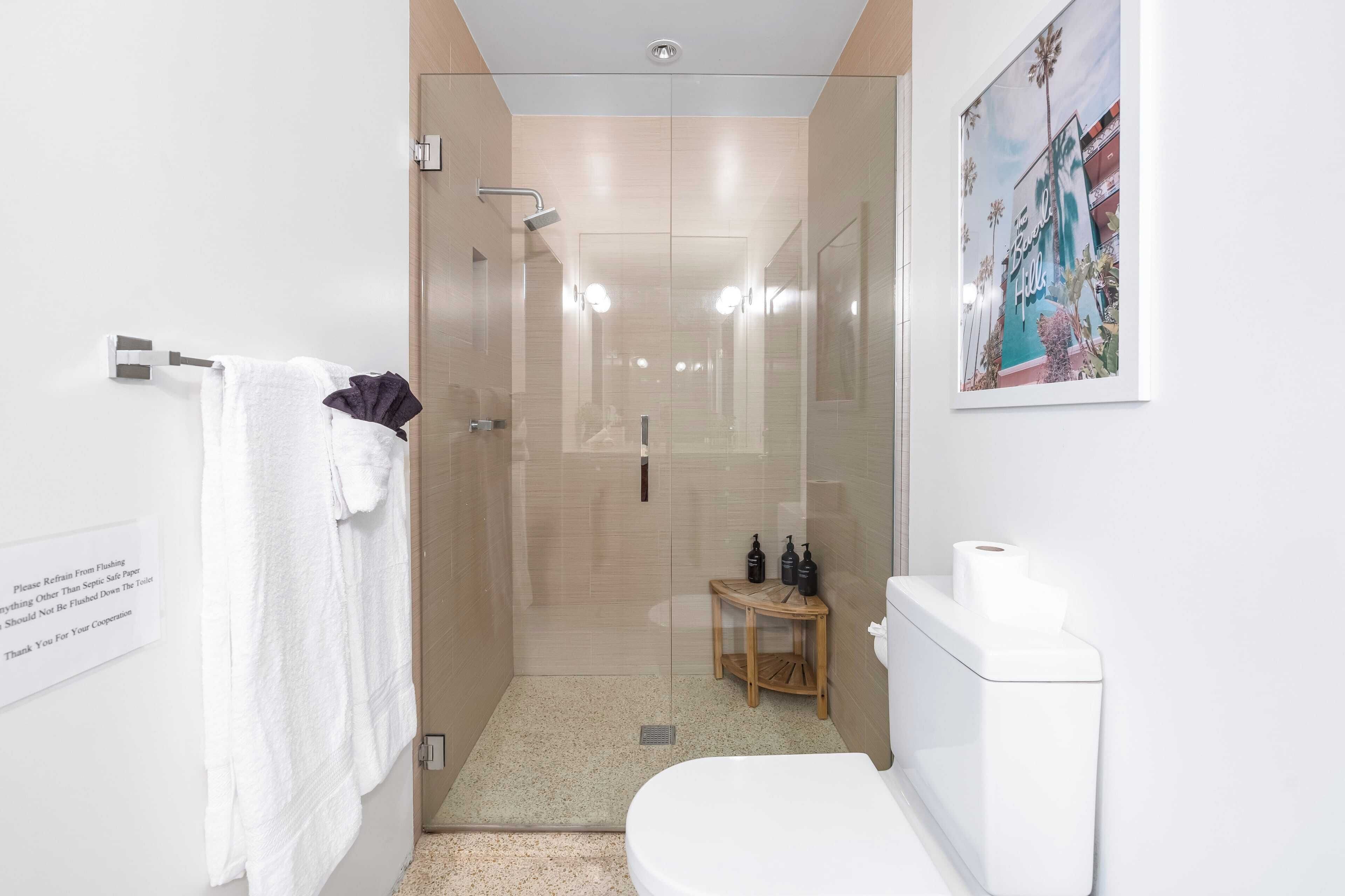 Ein modernes Badezimmer mit Duschkabine aus Glas, Toilette und einem kleinen Holztisch mit Pflegeartikeln.