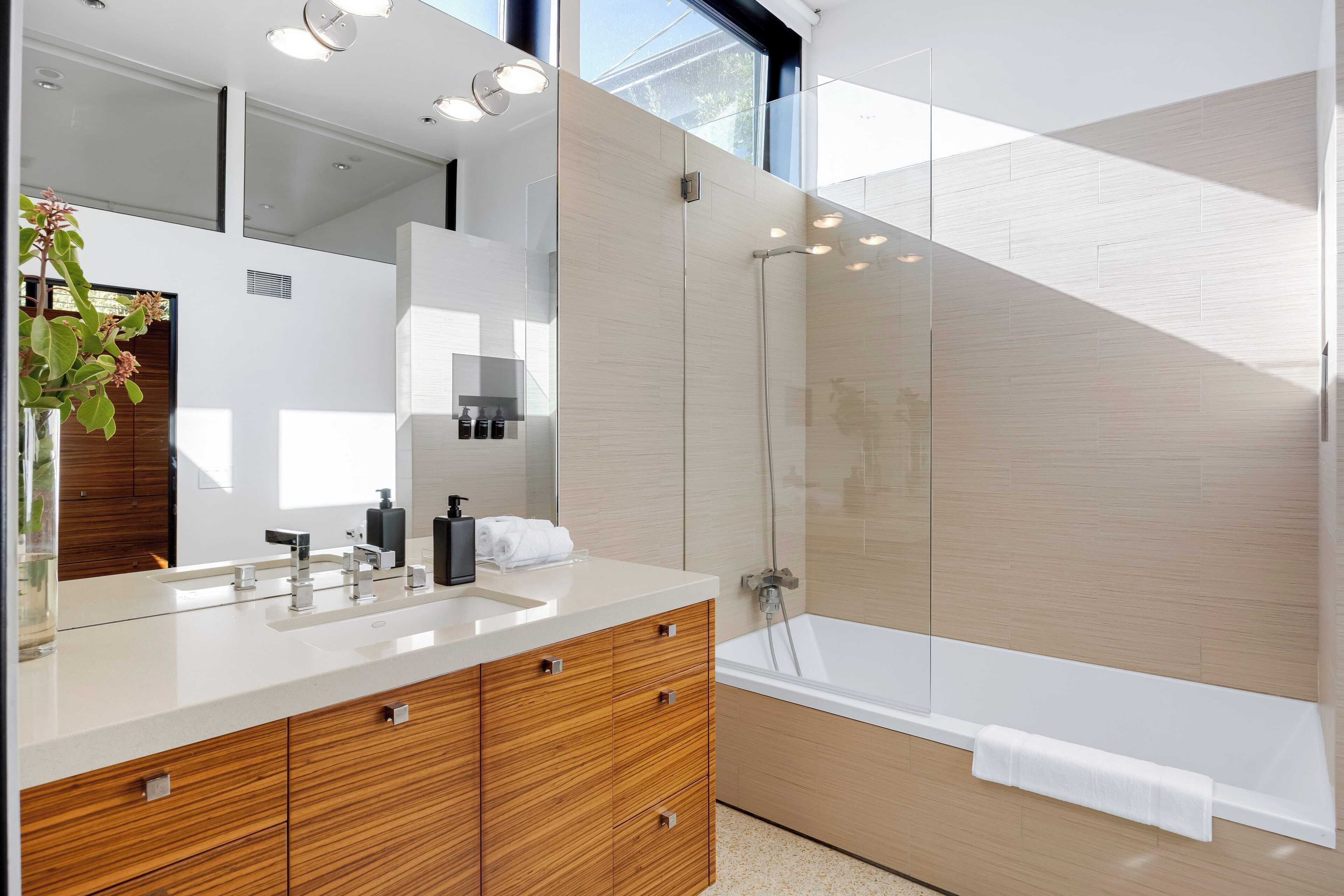 A modern bathroom with a large mirror, wooden vanity, white sink, and a glass-enclosed shower area.