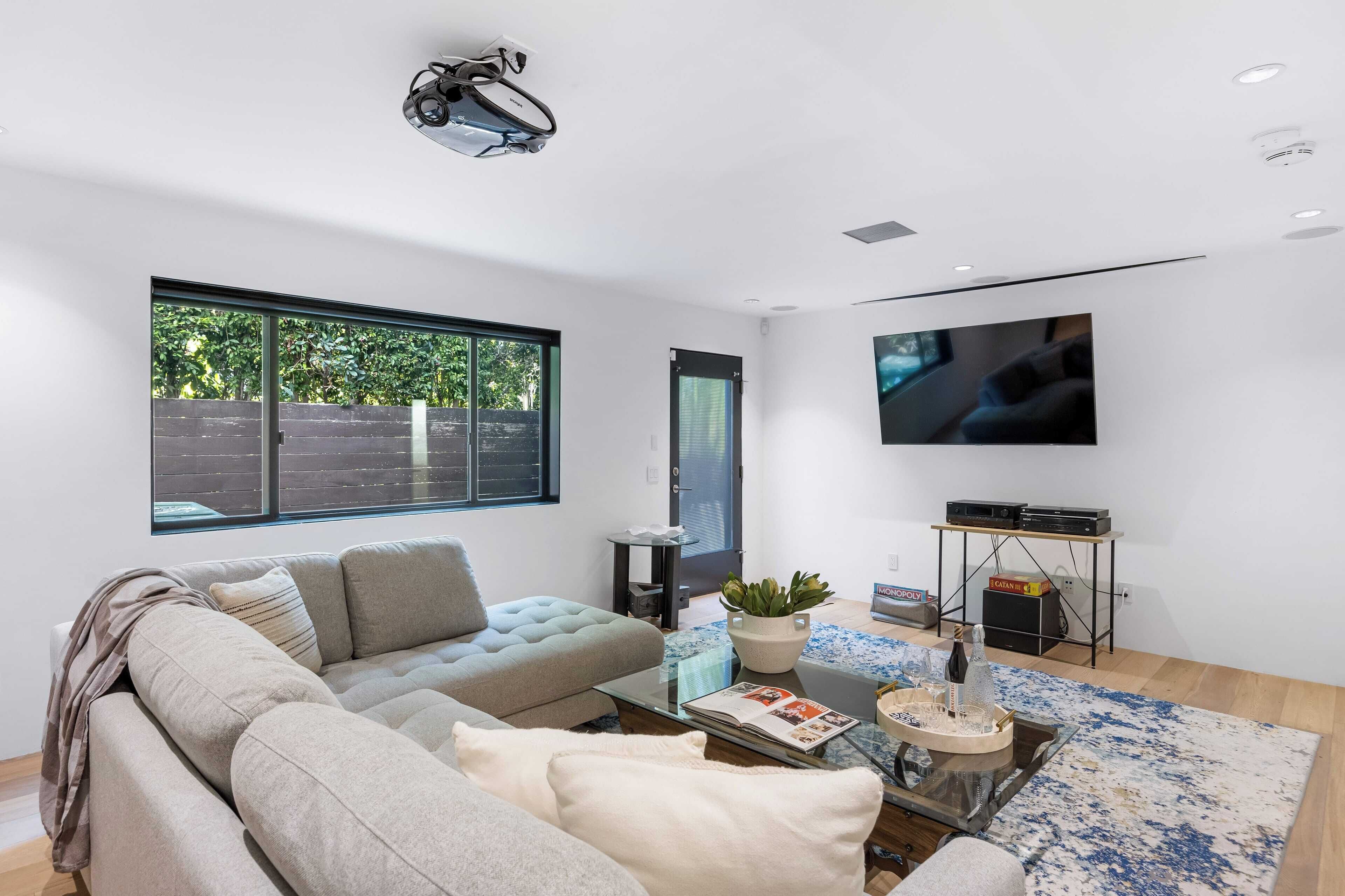 A modern living room with a large window, a flat-screen TV, a sofa, a coffee table, and a small side table.