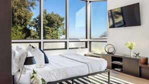 A modern bedroom with a large bed, a desk, and a TV.