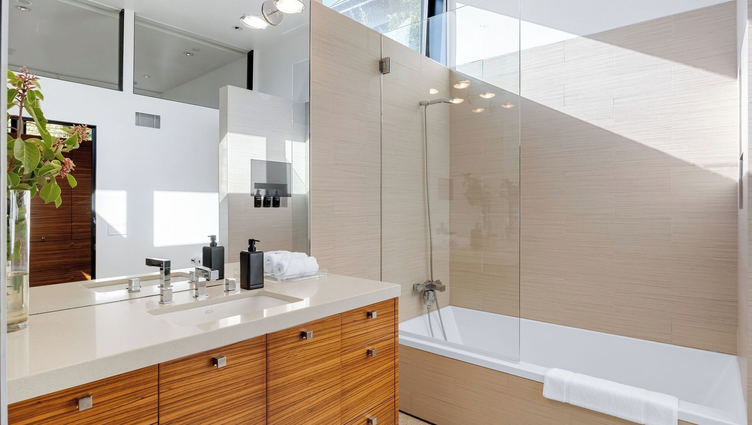 A modern bathroom with a large mirror, a sink with multiple faucets, a shower area, and wooden cabinetry.