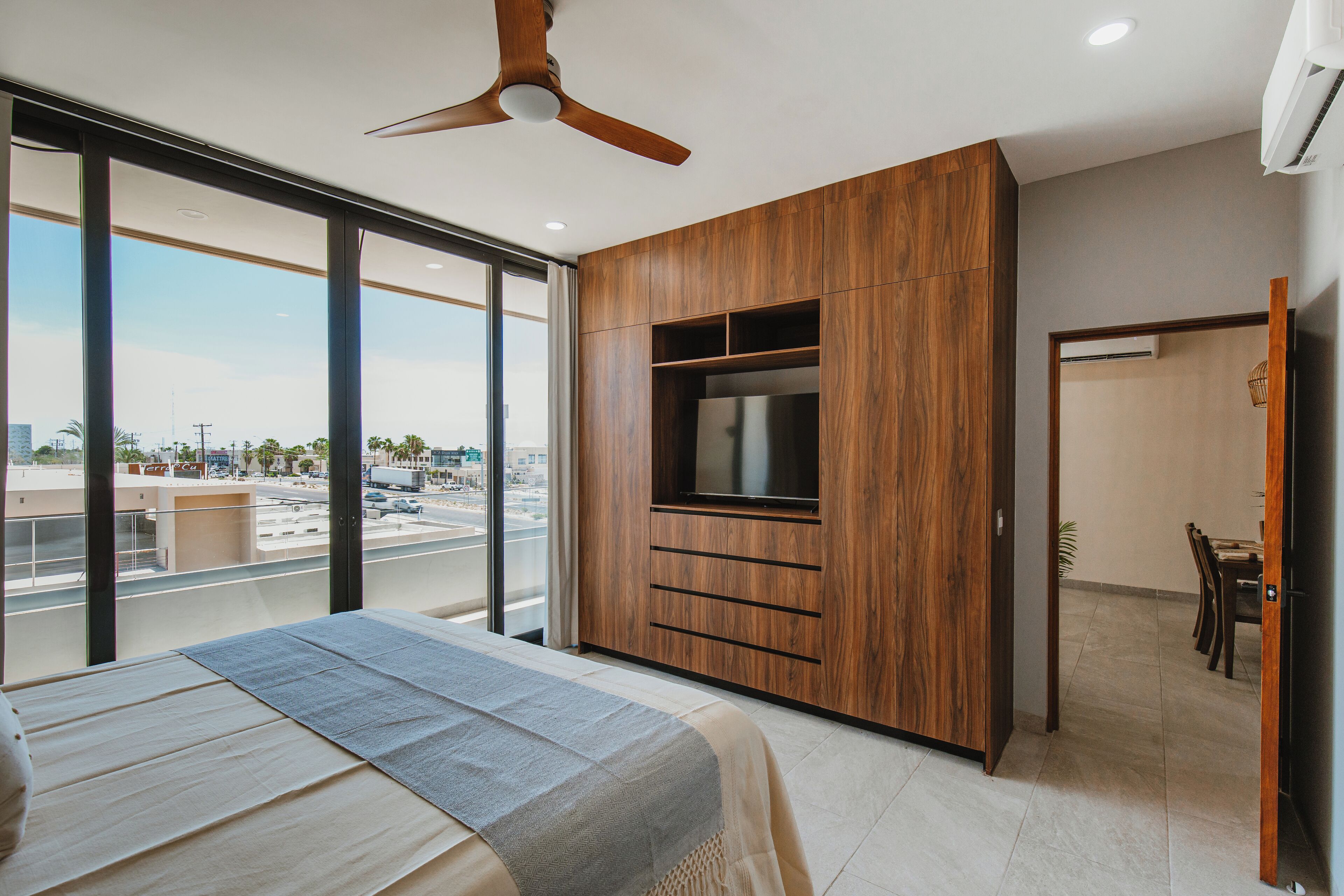 A modern bedroom with a large bed, a built-in TV, and a city view.