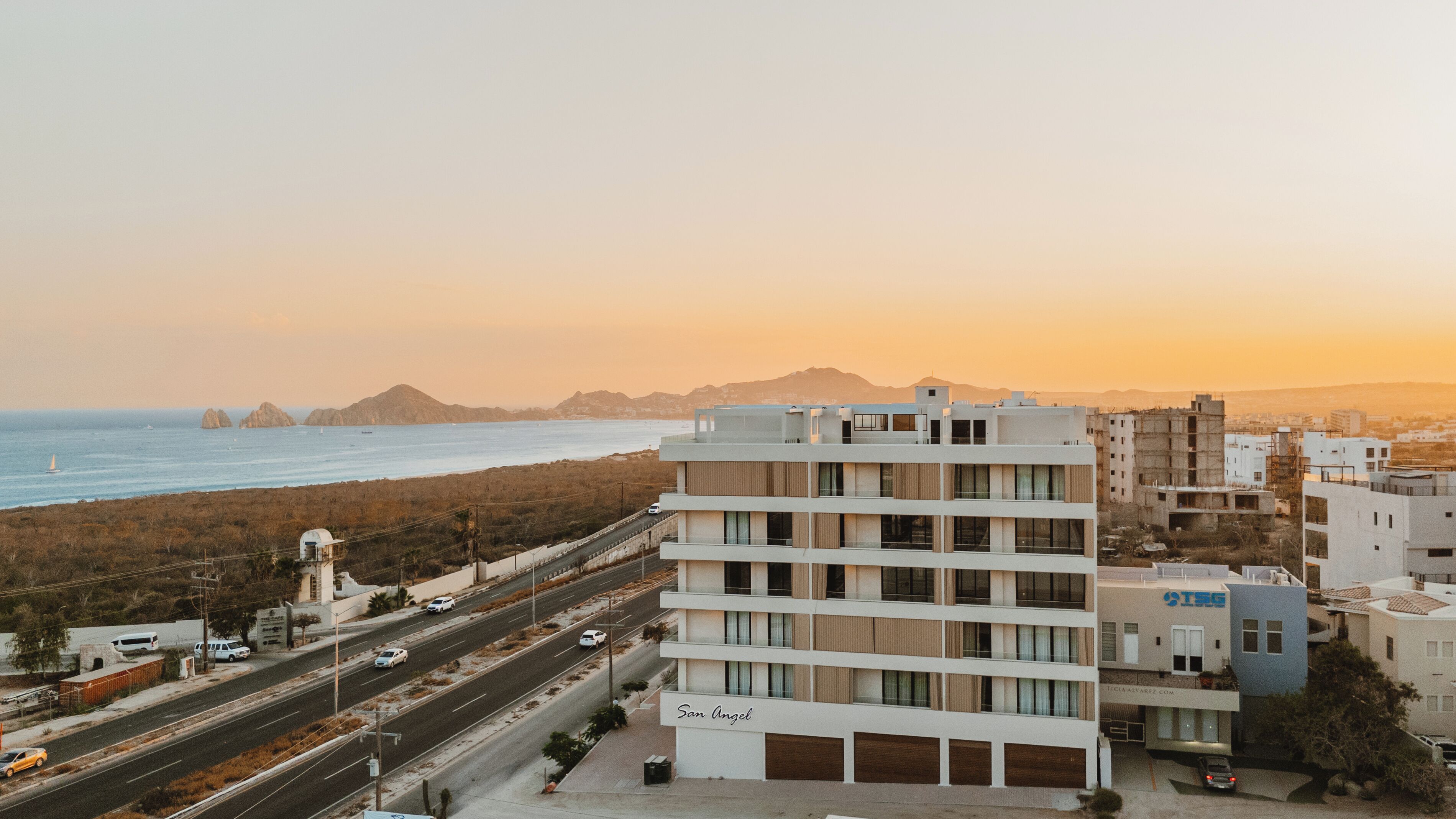 A multi-story hotel with a view of the sea and mountains in the background.