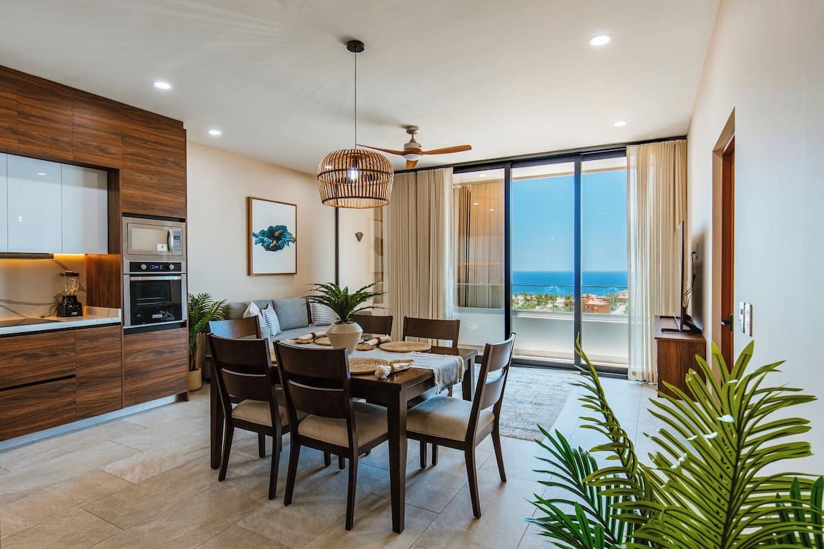 A modern kitchen with a built-in microwave and oven, a dining area with a table and chairs, and a large sliding glass door leading to a balcony with a view of the ocean.