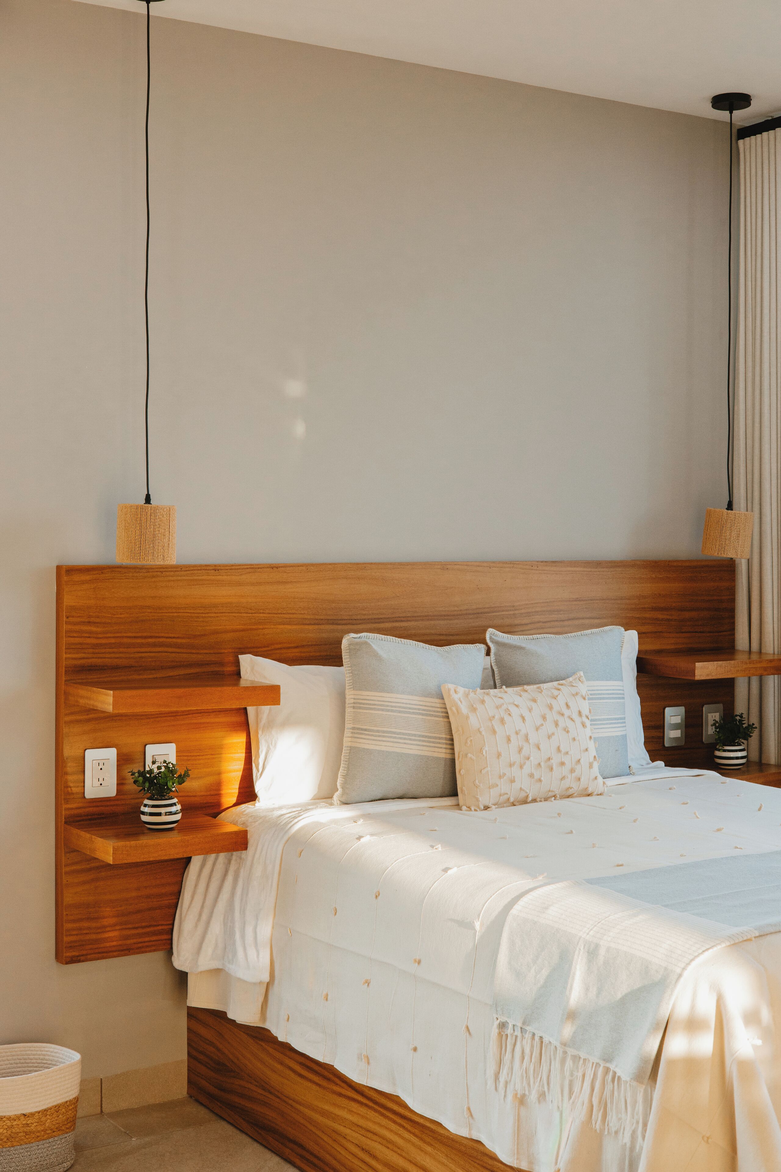 Une chambre à coucher avec une tête de lit en bois, un lit avec une literie blanche et une table de chevet agrémentée d’une plante.