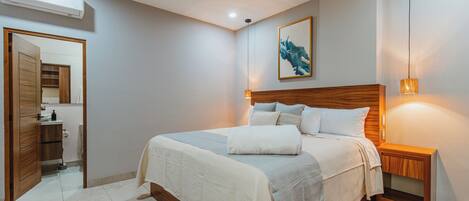 Quarto com cabeceira de madeira, cama com roupa de cama branca, mesa de cabeceira com abajur e ventilador de teto.