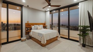 Camera da letto moderna con un letto grande, un ventilatore a soffitto e vista sulla città attraverso ampie finestre a tutta parete.